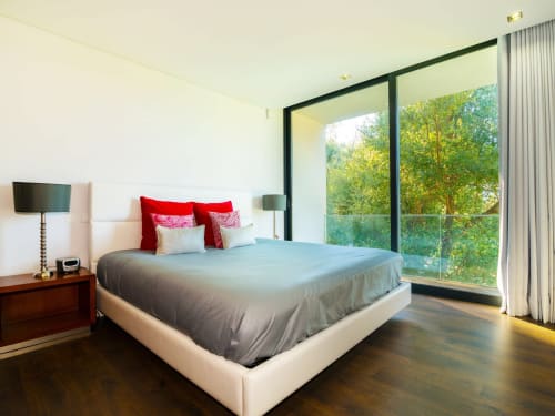 Quarto moderno da villa Casa da Luz Gerês com cama king, almofadas vermelhas e janelas panorâmicas com vista para a floresta verde