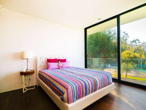 Quarto luminoso com cama de roupa de cama às riscas coloridas, amplas portas de vidro com vista para o rio e montanhas na Casa da Luz Gerês