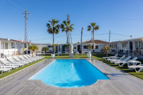 Bungalow Buda Beach pool area with blue swimming pool, loungers, palm trees, and bungalows in Chipiona