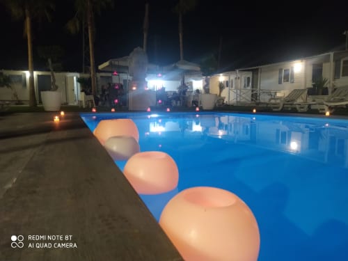 Illuminated pool at night with lounge floats, bungalows and palm trees at Bungalow Buda Beach, Chipiona