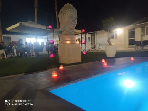 Night poolside at Bungalow Buda Beach in Chipiona with illuminated Buddha bust, red lanterns, and glowing pool