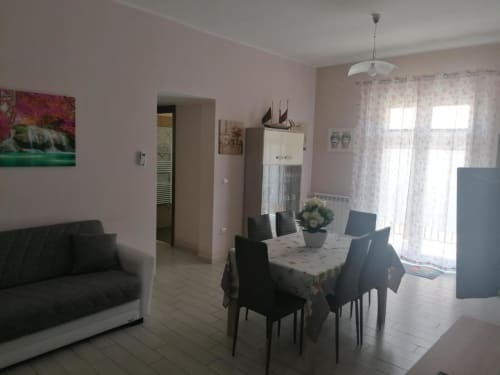 Moderno spazio living e zona pranzo a Licata con cucina, tavolo, divano e accesso al balcone