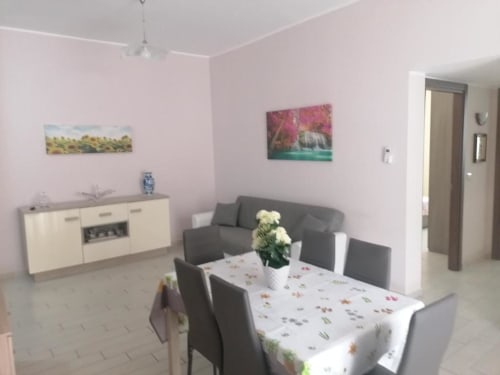 Ampia zona living open-plan con tavolo da pranzo, divano grigio, angolo cottura e dettagli rosa a La Maison Du Port, Licata