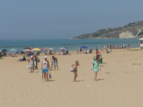 Spiaggia affollata di sabbia a Licata con bagnanti, ombrelloni e acque cristalline del Mediterraneo sotto cielo azzurro