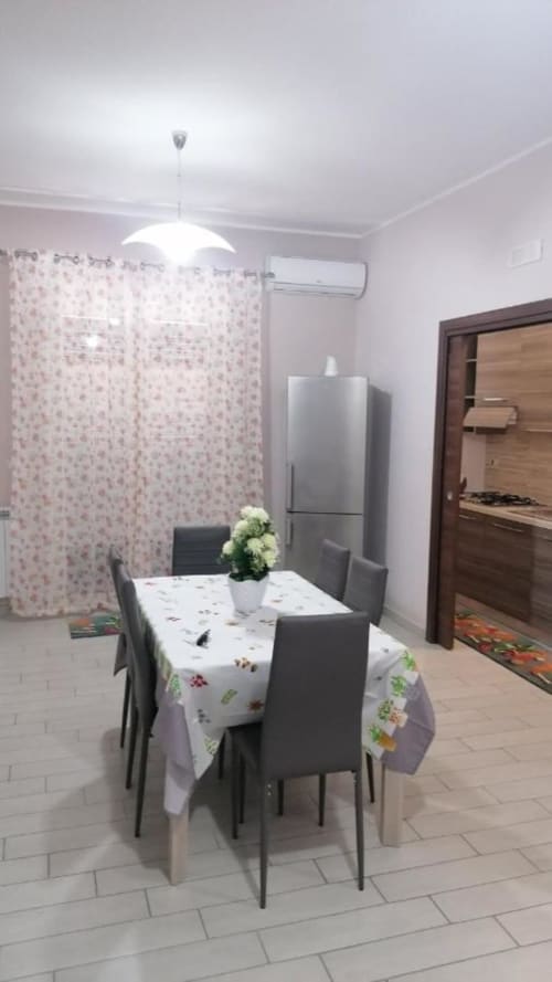 Modern dining room at La Maison Du Port hotel in Licata with table, chairs, pendant light, kitchenette and floral accents