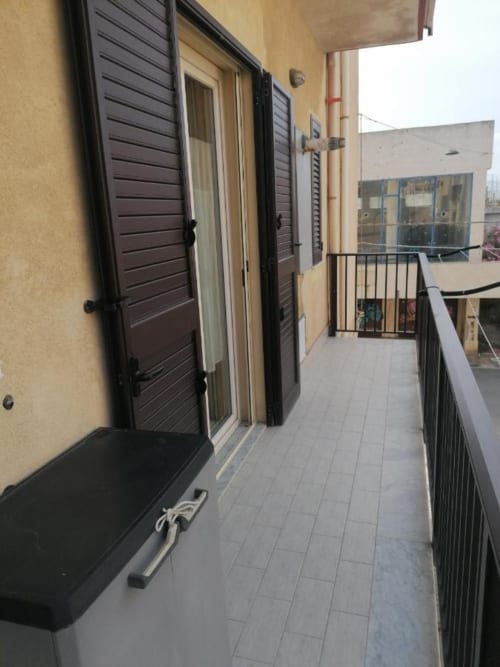 Balcony at La Maison Du Port hotel in Licata with tile flooring, shuttered doors, and black railing overlooking surrounding