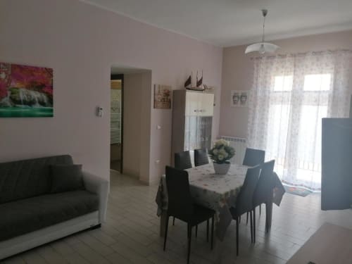 Spacious dining and living room at La Maison Du Port in Licata with dark sofa, dining table, and sheer curtains.