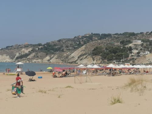Spiaggia di Licata con arenile sabbioso, ombrelloni colorati, bagnanti e edifici sulla scogliera