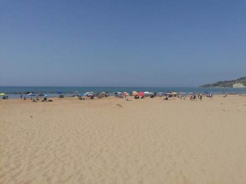 Busy Licata beach with colorful umbrellas and sunbathers on sandy shore