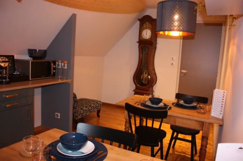 Coin repas chaleureux à la Théière & Couverts B&B de Cernay avec table en bois, chaises noires et horloge de parquet vintage.