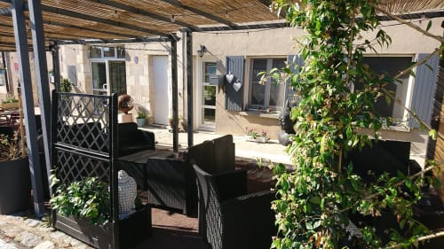 Coin terrasse ombragé de l'hôtel Les Deux Porches à Verrières avec chaises noires, plantes grimpantes et accès à la cour