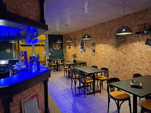 Café contemporain aux Deux Porches à Verrières avec murs en liège, chaises jaunes, suspensions et comptoir bar éclairé de bleu