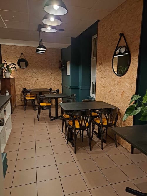 Zone de restauration contemporaine de l'hôtel Les Deux Porches à Verrières avec tables noires, chaises moutarde, murs en liège et style industriel