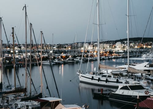 Barche a vela ormeggiate nel porto di Alghero con edifici sul lungomare al tramonto