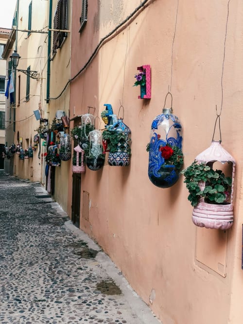 Affascinante vicolo di Alghero con vasi sospesi creativi su muro in terracotta