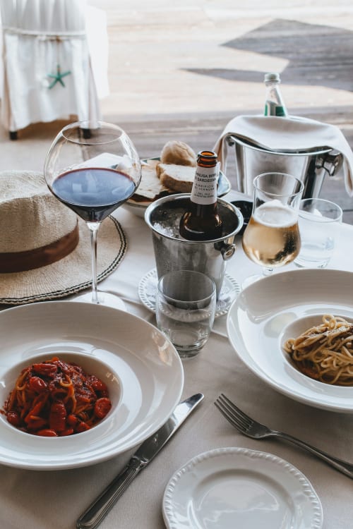 Cena sul mare a Catalogna10 ad Alghero: piatti di pasta, vino rosso e vedute marine da un tavolo di ristorante mediterraneo.