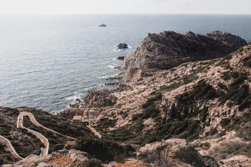 Scogliere costiere panoramiche e strada sinuosa vicino ad Alghero con mare turchese e isole rocciose