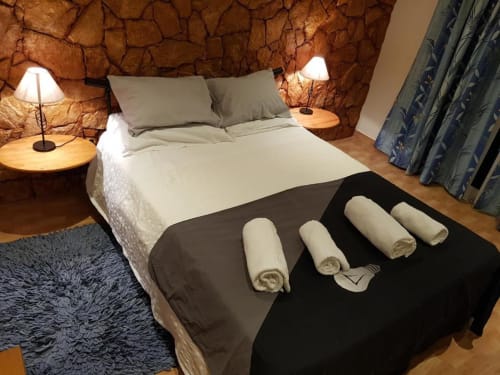 Habitación doble Ocean View Lagos con muro de acento de piedra, cama con toallas enrolladas, lámparas de mesita y cortinas con vistas al jardín