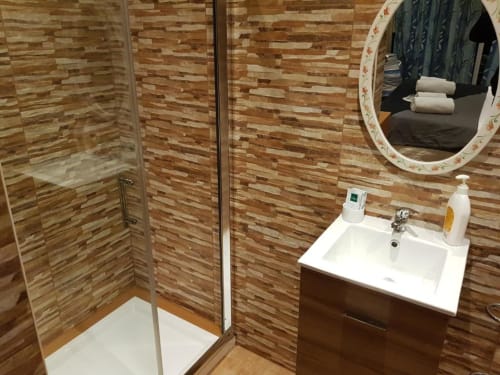 Baño moderno del hostel Ocean View Lagos con azulejos de madera y ladrillo, cabina de ducha, lavamanos blanco, espejo ovalado y artículos de aseo