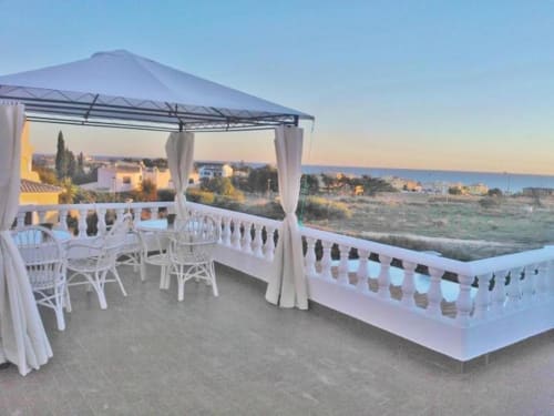 Ocean View Lagos terrace at sunset with white chairs, pergola, and sea vista overlooking coastal town