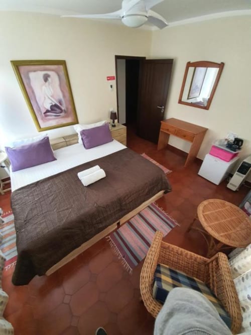 Habitación doble en el hostal Ocean View Lagos con cama queen, detalles en púrpura, muebles de madera y sillas de ratán en terraza
