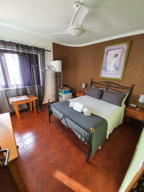 Habitación doble en el hostal Ocean View Lagos con cama de estructura metálica, piso de terracota, paredes marrones, ventilador de techo y vista al jardín