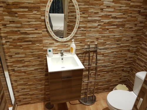 Baño moderno del albergue Ocean View Lagos con paredes de azulejos de madera, lavabo blanco, espejo redondo, inodoro y toallero