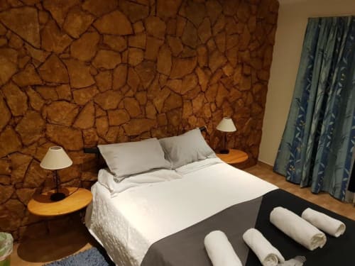 Habitación doble en el hostal Ocean View Lagos con pared de corcho, ropa blanca, toallas enrolladas, mesitas de madera y cortinas color azul verdoso