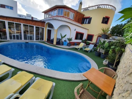 Ocean View Lagos hostel pool with yellow loungers, colorful architecture, and tropical gardens in Portugal