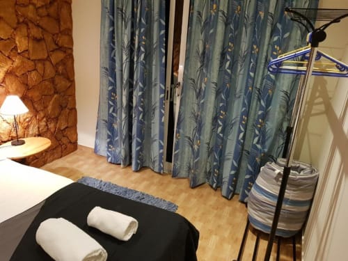 Habitación doble en el hostal Ocean View Lagos con cama, cortinas florales azules, piso de madera, lámpara de escritorio y perchero
