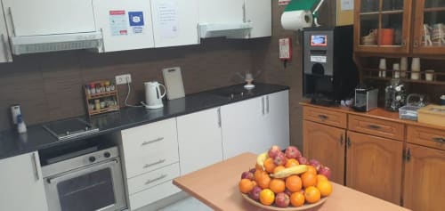 Cozinha do hostel Sunny House em Lagos com armários brancos, bancadas pretas, armazenamento em madeira e tigela de frutas frescas na mesa