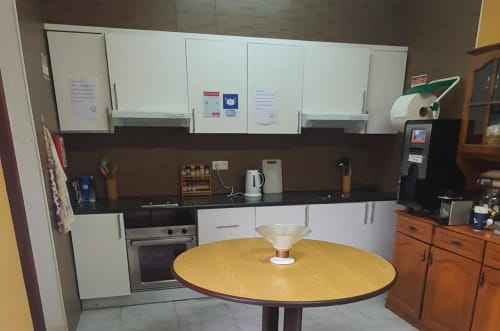 Cozinha moderna na pousada Sunny House em Lagos com armários brancos, mesa redonda amarela e eletrodomésticos em aço inoxidável