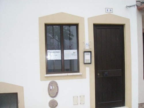 Entrada do albergue Sunny House em Lagos com janela de recepção, porta de madeira escura e interfone em fachada bege