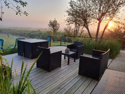 Terrasse au coucher de soleil aux Gîtes De La Grande Borderie avec mobilier noir, terrasse en bois, rivière et arbres à Saint-Gervais
