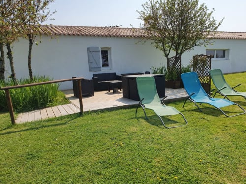 Terrasse extérieure de la villa Gites De La Grande Borderie à Saint Gervais avec chaises longues, terrasse en bois et bâtiment chaulé