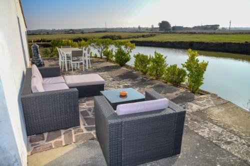Terrasse au bord de l'eau aux Gites De La Grande Borderie avec mobilier en rotin, table à manger et vue sur la campagne près de Saint Gervais