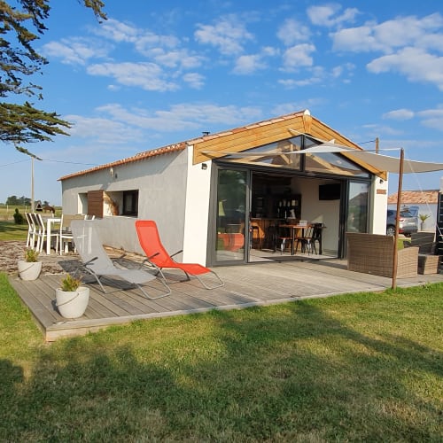 Villa moderne aux Gîtes De La Borderie à Saint Gervais avec terrasse en bois, transats, coin repas et portes-fenêtres ouvertes