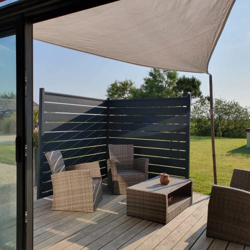 Terrasse extérieure de la villa Gites De La Grande Borderie avec mobilier en rotin, voile d'ombrage et écrans de confidentialité noirs surplombant