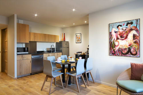 Cuisine-salle à manger du Lodge VIP moderne à AJOUCADOU Lourmarin avec armoires en bois, chaises bleues et œuvres d'art colorées