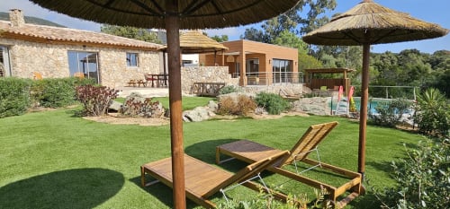 Villas-Majos villa in Porto-Vecchio with wooden loungers under thatched umbrella, lush gardens and stone buildings