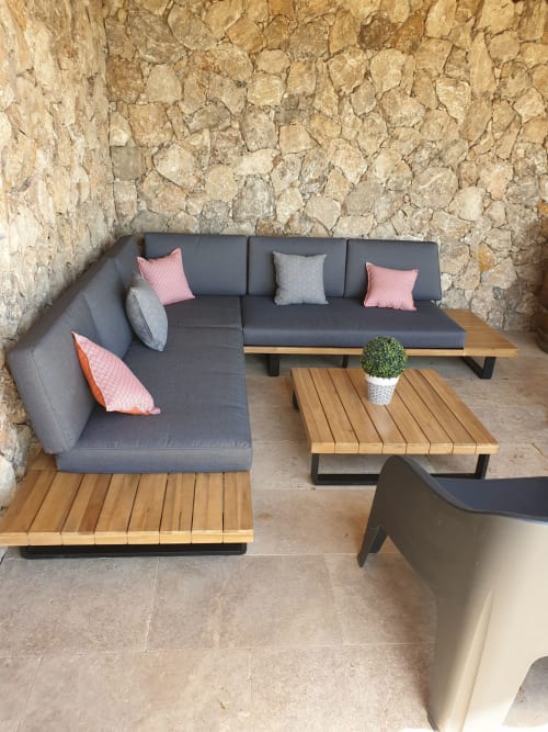 Zone de détente extérieure à la villa Villas-Majos avec canapé gris en L, tables en bois et mur en pierre