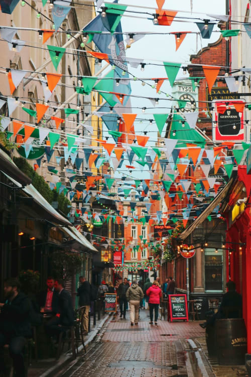 Colorful Irish flag bunting decorates a bustling Dublin street lined with historic pubs and shops