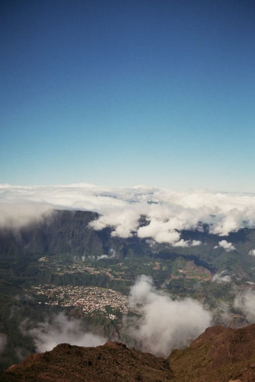 Vue aérienne de la vallée de Cilaos avec nuages, montagnes et pentes boisées à Au pied des Sources