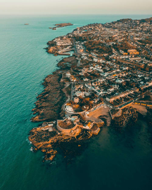 Aerial coastal view of Dublin with turquoise waters, rocky cliffs, and hillside buildings