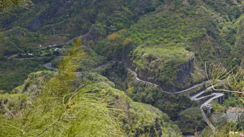 Vue aérienne d'une route sinueuse traversant une forêt dense près de Cilaos, l'hôtel Au pied des Sources niché dans la vallée