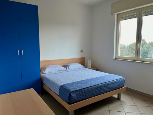 Camera da letto moderna nell'appartamento di Tirrenia con letto matrimoniale, armadio blu e ampie finestre che affacciano sul verde