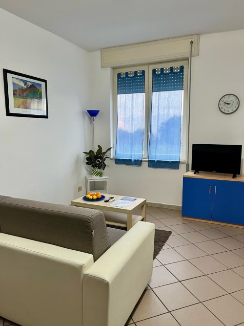 Moderna zona living dell'Apartment Tirreno a Tirrenia con divano grigio, TV, persiane blu e pavimenti in cotto