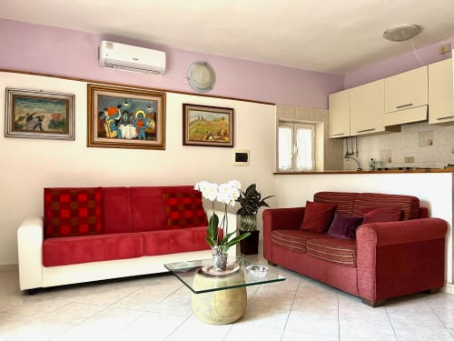 Soggiorno moderno a due livelli a Tirreno con divani rossi e bianchi, tavolo in vetro, opere d'arte incorniciate e zona cucina