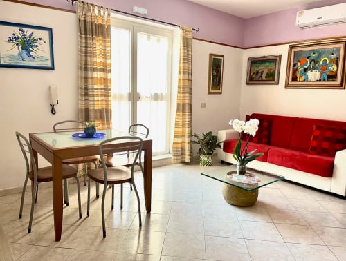 Luminoso soggiorno dell'Apartment Tirreno a Tirrenia con divano rosso, tavolo da pranzo e porte-finestre