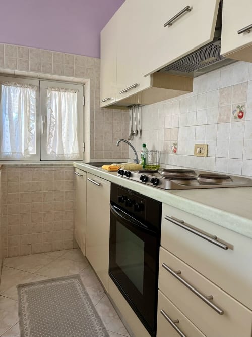 Cucina moderna dell'Apartment Tirreno a Tirrenia con mobili bianchi, fornello nero e rivestimento beige